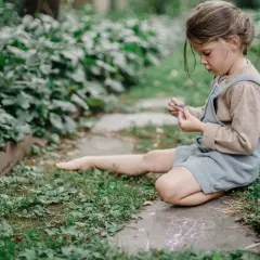 Dziecko rysuje kredą na chodniku. To właśnie co to znaczy być kreatywnym – tworzyć piękno z niczego, w otoczeniu natury.