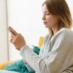 Młoda kobieta z telefonem w dłoni, siedząca na kanapie. Nie porównuj się z innymi, skup się na sobie.