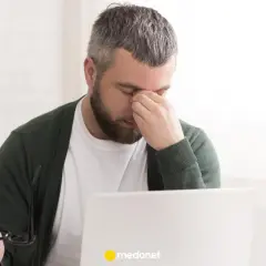 Mężczyzna z zespołem pustego siodła masuje oczy, siedząc przy laptopie.