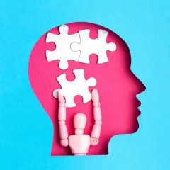Drewniany ludzik układa puzzle w głowie, symbolizując otwarty umysł i proces myślowy.