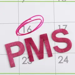 Litery PMS na kalendarzu, dzień 16 zaznaczony kółkiem. Symbolizuje to objawy przed okresem, które mogą pojawić się w tym czasie.