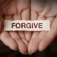 Dłonie trzymające skrawek papieru z napisem "FORGIVE". To symbol tego, co to znaczy wybaczyć – uwolnić się od urazy i otworzyć na pojednanie.