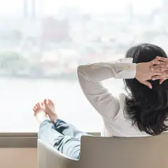 Kobieta w białej koszuli odpoczywa, ręce za głową, nogi wyciągnięte. To obraz psychologicznej homeostazy i spokoju.