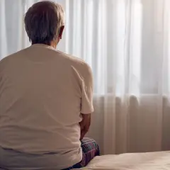 Starszy mężczyzna siedzi na łóżku, patrząc przez okno. Zastanawia się nad tym, co nas zabija i co sprawia, że żyjemy wiecznie.