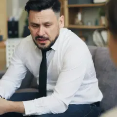 Mężczyzna w białej koszuli i krawacie, trzymający okulary, zastanawia się, jak inteligentnie zakończyć rozmowę.