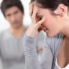 Kobieta z ręką na czole, zmęczona kłótnią z partnerem, który wyciąga ręce. Osoba zaborcza cechy.