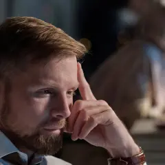 Zamyślony mężczyzna z zarostem, opierający czoło na dłoni, pokazuje, jak reaguje zraniony facet.
