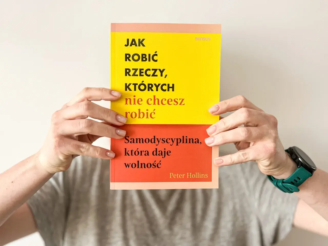 Dwie ręce trzymają książkę "Jak robić rzeczy, których nie chcesz robić". Na okładce hasło: "Samodyscyplina, która daje wolność".